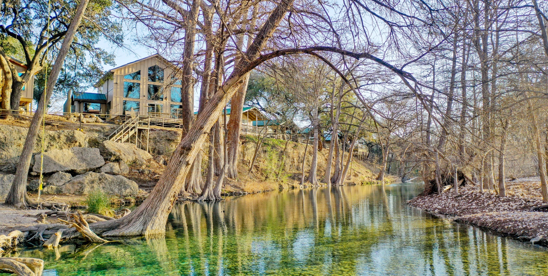 Clear green water of the Frio River beneath cypress trees, with River Bluff cabins perched on the limestone bluff
